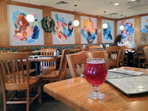 A glass of cranberry cider in front of some tables and large abstract art pieces on the walls