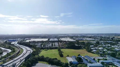 An ariel photograph looking out over Hendra, towards Pinkenba and the ocean. The sky is blue, with some fluffy white clouds, and a bright sun
