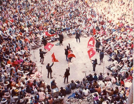 Photo of crowd of people around sever figures with communist flags, from the linked article