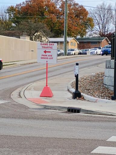 A portable "GAME DAY TRAFFIC GO THAT WAY" sign sitting directly in the middle of the sidewalk blocking wheelchair access.